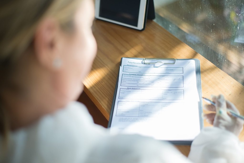 Someone filling in an application form by hand at a sunlit desk.