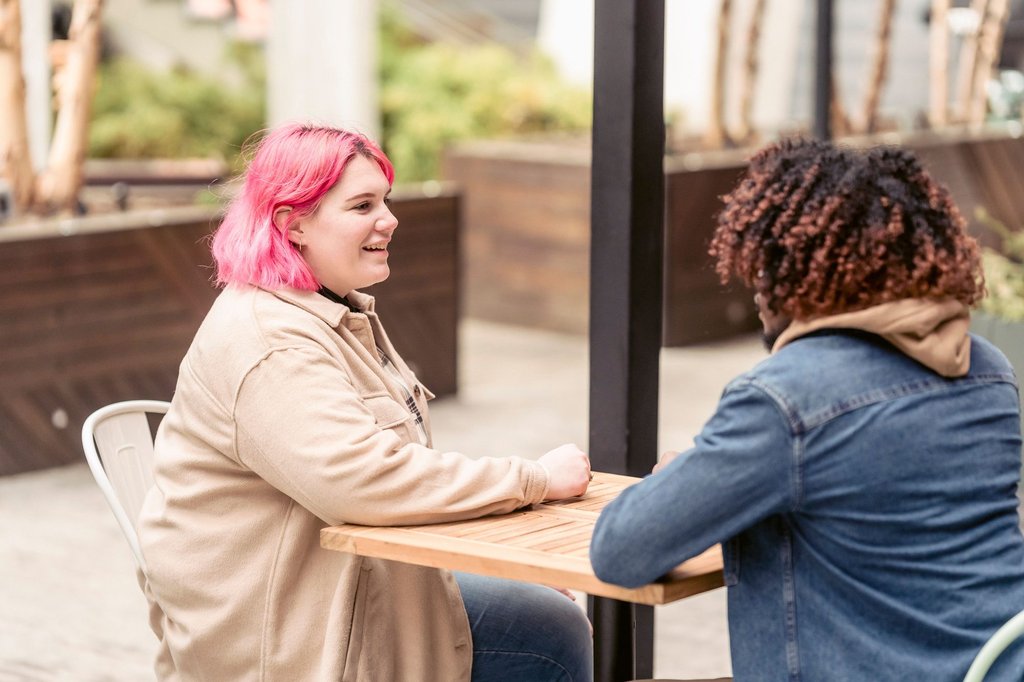 Two people in conversation over coffee at an outdoor cafe table.