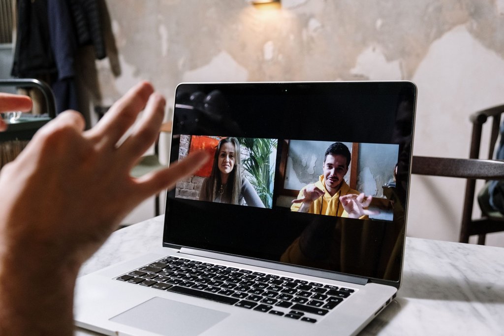 Someone on a laptop video call, gesturing through a point with a remote colleague.