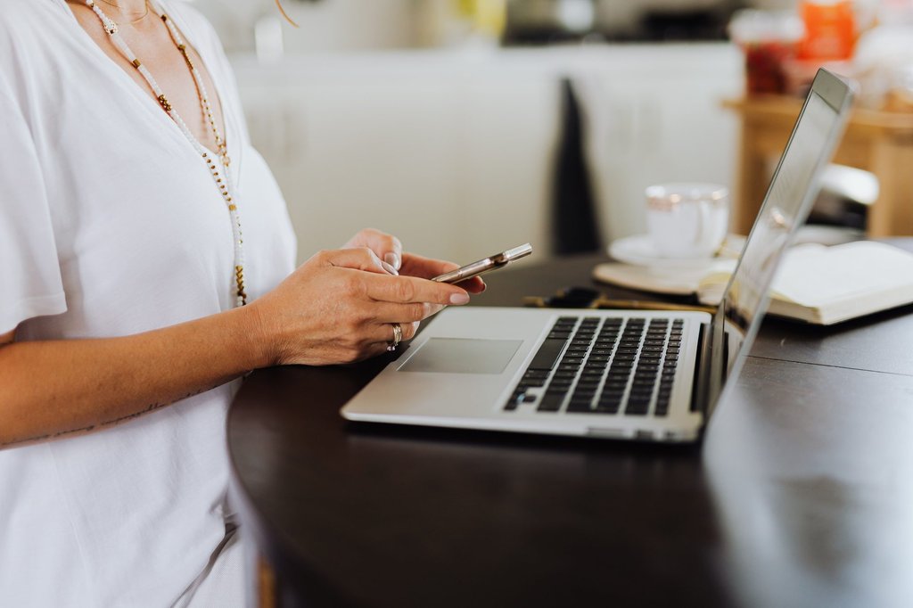 Checking messages on a phone beside an open laptop in a home office.