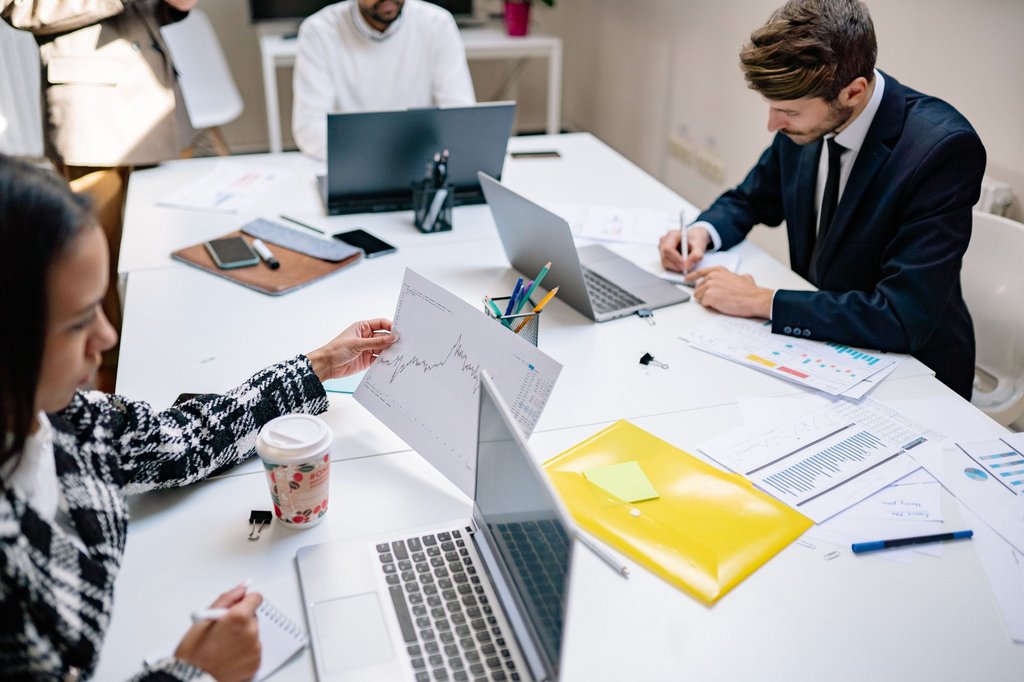Professionals collaborating over laptops and printed documents while planning a Zoho Campaigns email programme.
