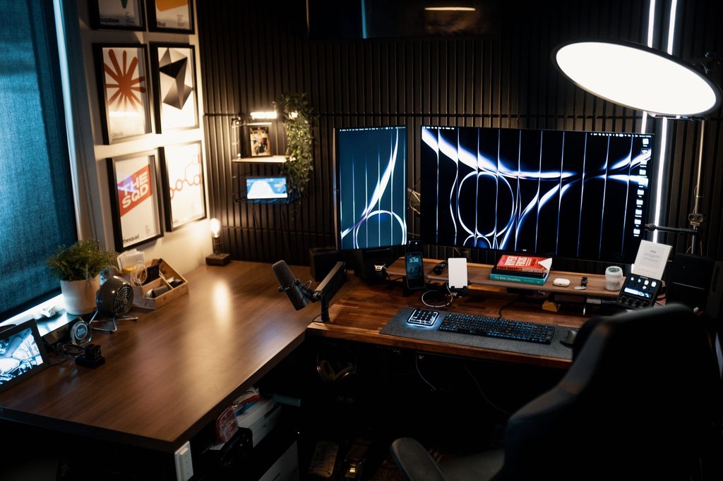 A desk with two monitors running side by side in a dim home office.