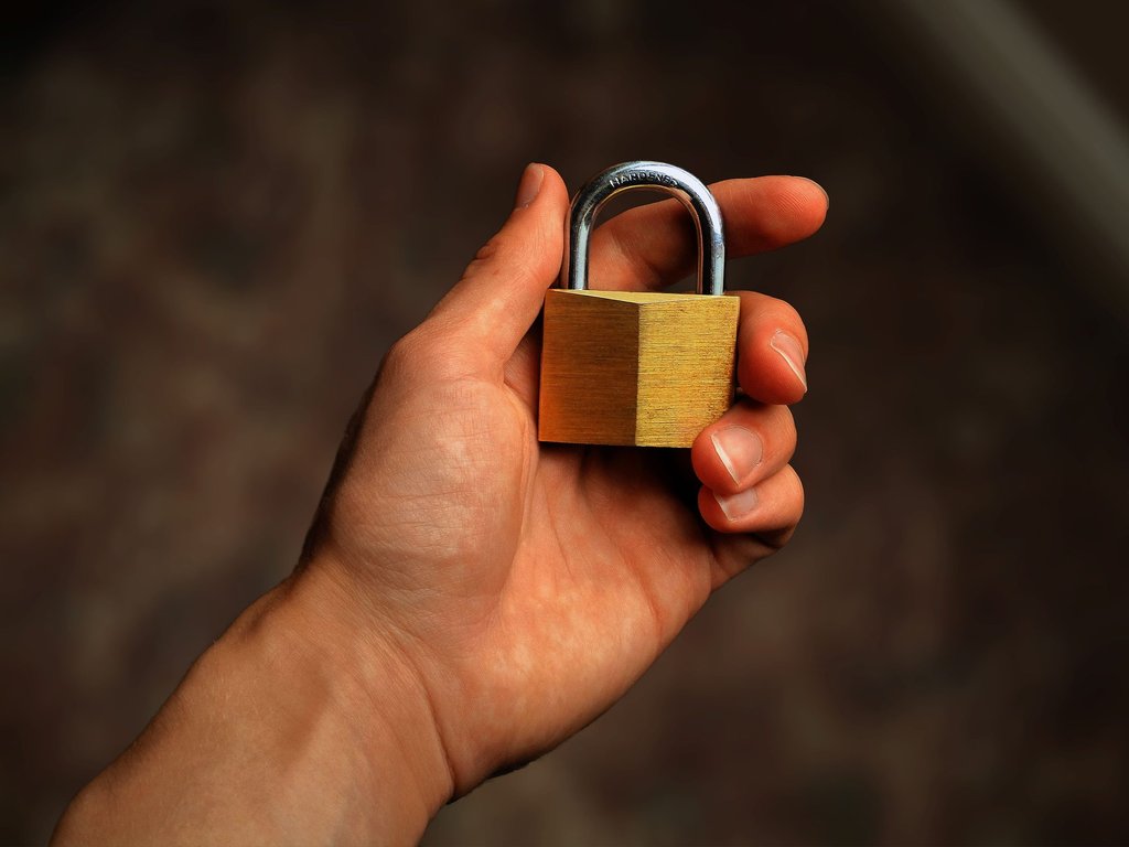 A hand holding a brass padlock, standing in for the credential security Zoho Vault manages for a team.