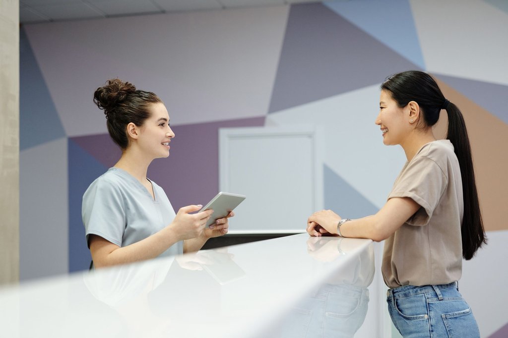 A receptionist greeting a visitor at a front desk and checking them against the day booking list.