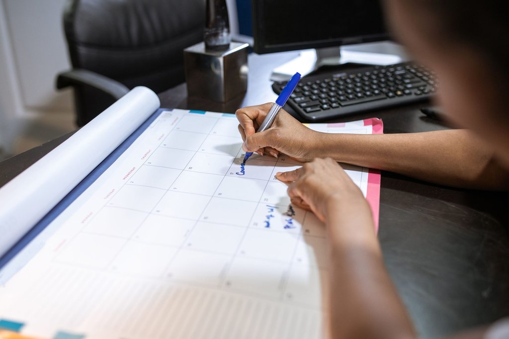 A wall calendar and a notebook on a desk while someone blocks out appointment slots for the week ahead.