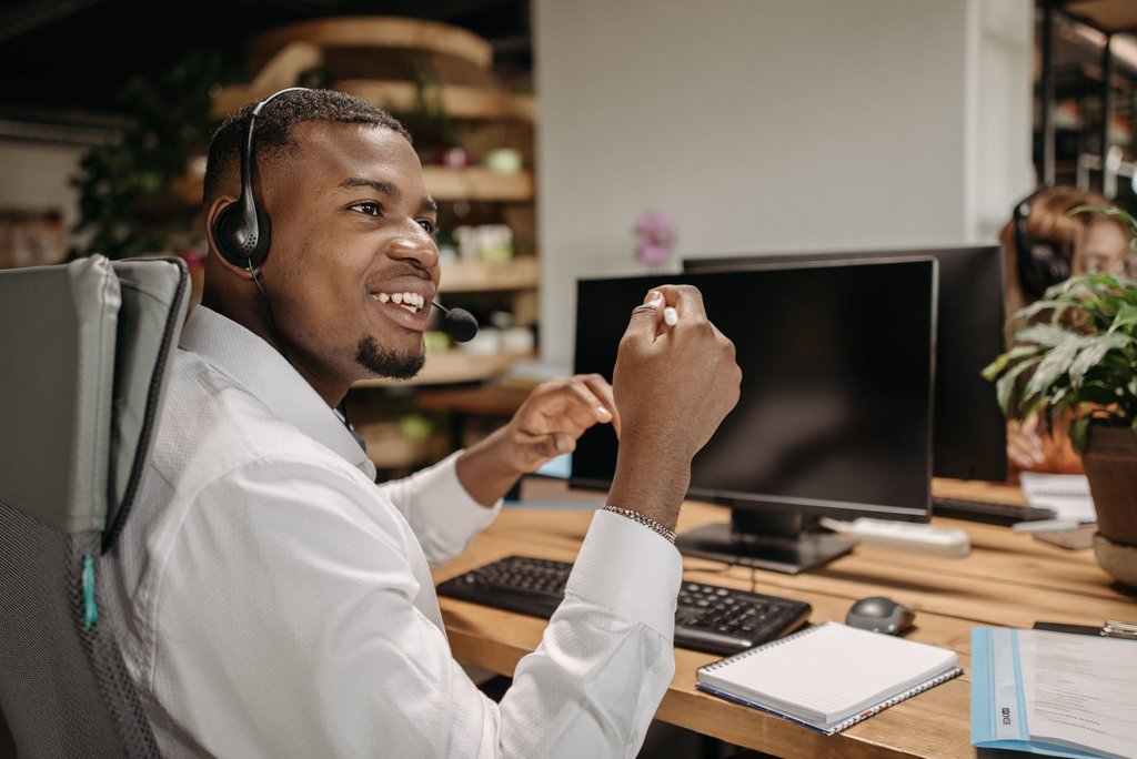 A support specialist in a headset working a ticket queue in a shared office.