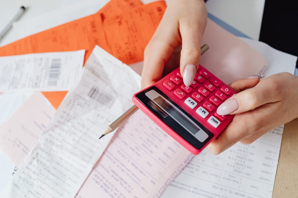 Hands working a calculator among receipts and paperwork, the manual expense process Zoho Expense replaces.