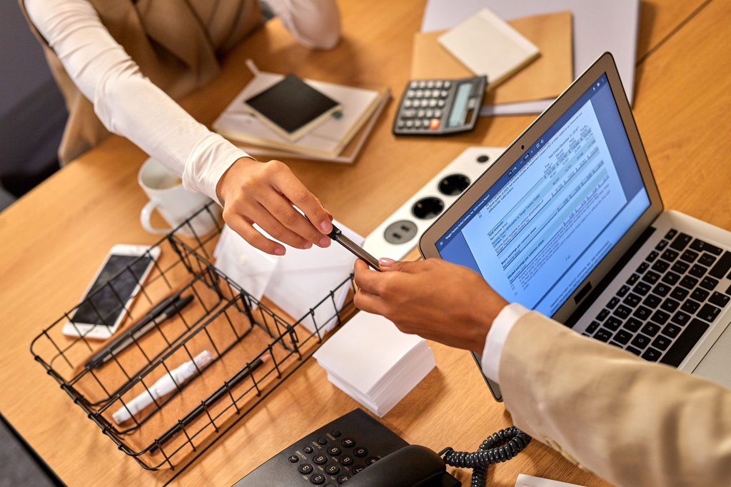Two professionals passing documents across a desk, the handoff Zoho WorkDrive turns into controlled file sharing.