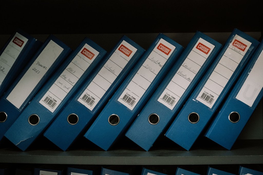 Labelled office binders arranged on a shelf, the filing structure Zoho WorkDrive replaces with shared cloud folders.