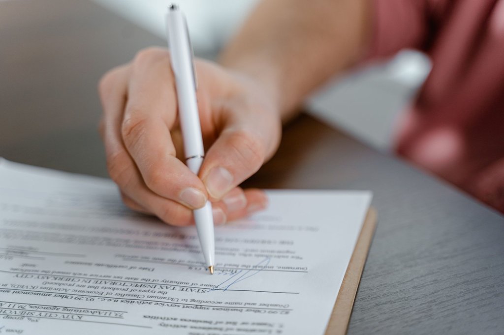 A hand signing an official document with a ballpoint pen, the step Zoho Sign moves into a tracked digital workflow.