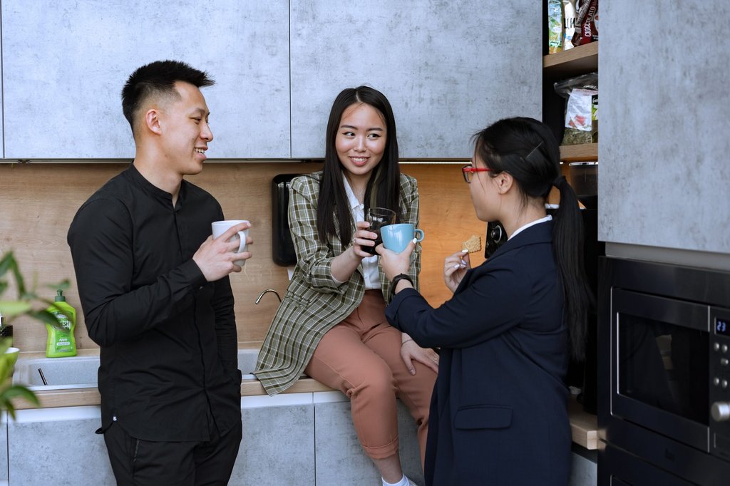 Two colleagues talking over coffee in an office kitchen, the exchange a team chat tool has to carry when nobody shares a building.