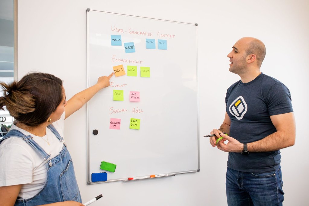 Two colleagues planning a project on a whiteboard covered in sticky notes.