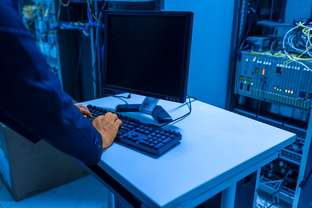 A technician at a terminal beside a rack of network equipment