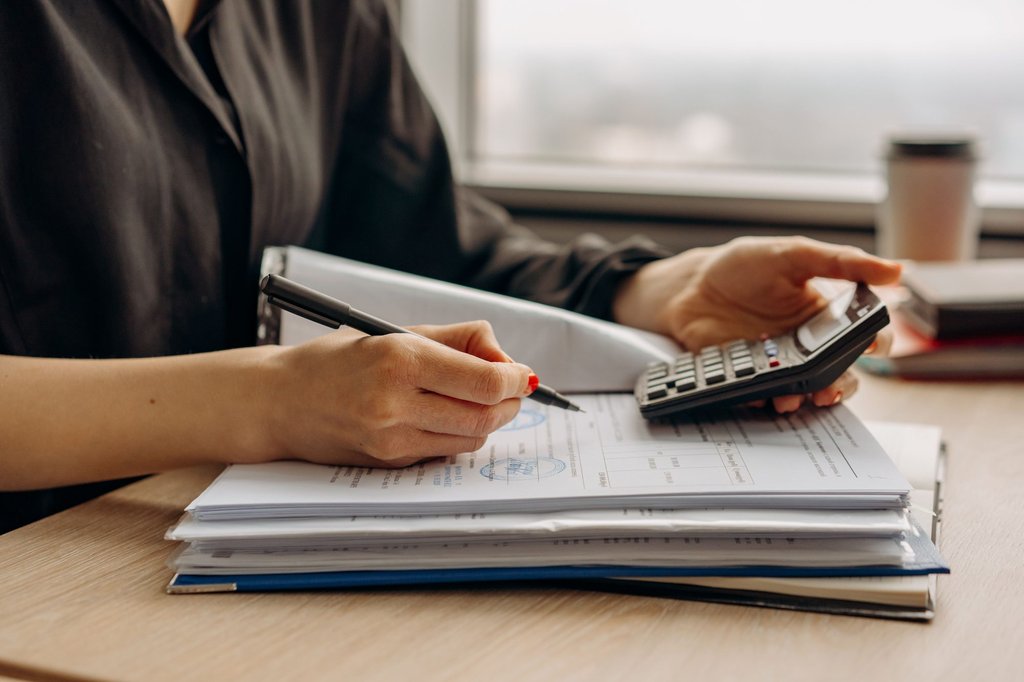 Hands checking figures on a calculator against a stack of invoices